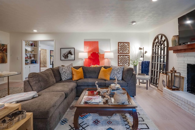 living room with a brick fireplace, a textured ceiling, and light wood-type flooring