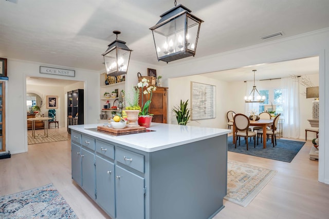 kitchen featuring pendant lighting, a kitchen island, ornamental molding, blue cabinets, and light wood-type flooring