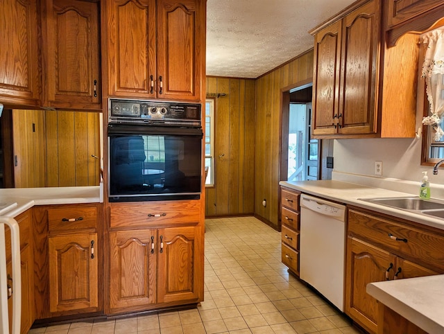 kitchen with sink, white dishwasher, black oven, a textured ceiling, and wooden walls