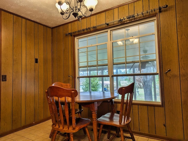 dining space with ornamental molding, light tile patterned flooring, a textured ceiling, wooden walls, and a chandelier