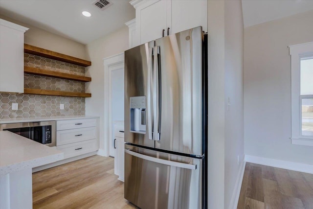 kitchen with tasteful backsplash, stainless steel fridge, white cabinets, and light wood-type flooring