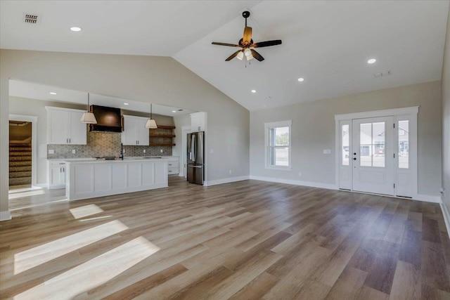 unfurnished living room with high vaulted ceiling, ceiling fan, and light wood-type flooring