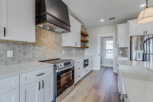 kitchen featuring premium range hood, decorative light fixtures, appliances with stainless steel finishes, light stone countertops, and white cabinets