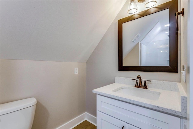 bathroom featuring vanity, hardwood / wood-style floors, vaulted ceiling, and toilet