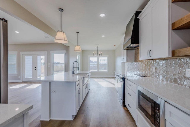 kitchen featuring premium range hood, stainless steel range with electric stovetop, a kitchen island with sink, black microwave, and white cabinets