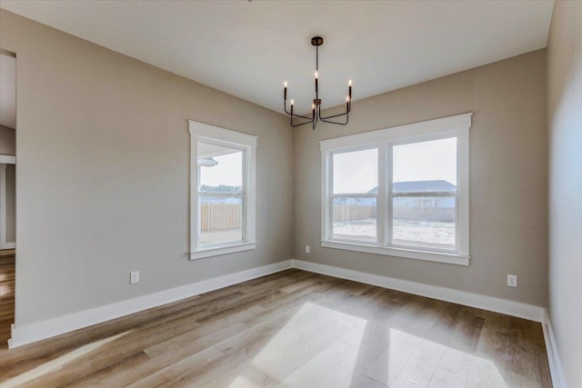 unfurnished room featuring a notable chandelier and light hardwood / wood-style flooring