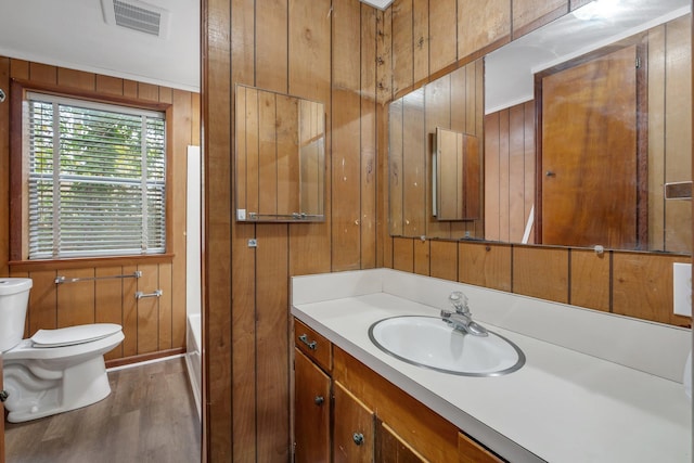 bathroom with wood walls, crown molding, wood-type flooring, toilet, and vanity