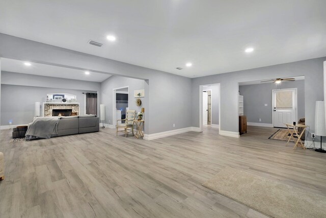 living room featuring light wood-type flooring, a brick fireplace, and ceiling fan