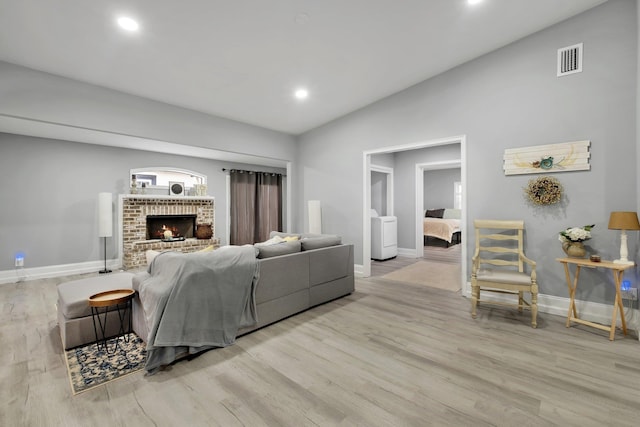 living room with a brick fireplace, light hardwood / wood-style flooring, and vaulted ceiling