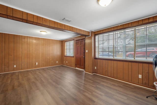 empty room featuring wooden walls, crown molding, and dark wood-type flooring