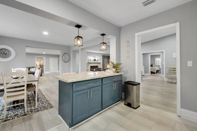 kitchen featuring pendant lighting, light stone countertops, a fireplace, blue cabinetry, and kitchen peninsula