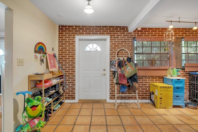 tiled foyer featuring beamed ceiling and brick wall