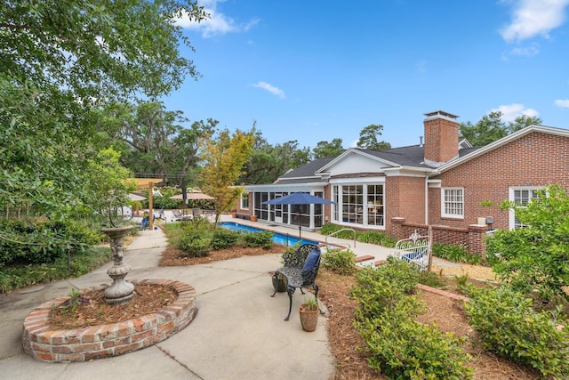 back of house with an outdoor pool, a patio area, a chimney, and brick siding