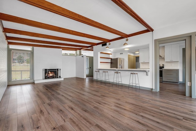 unfurnished living room featuring a large fireplace, wood-type flooring, and beam ceiling