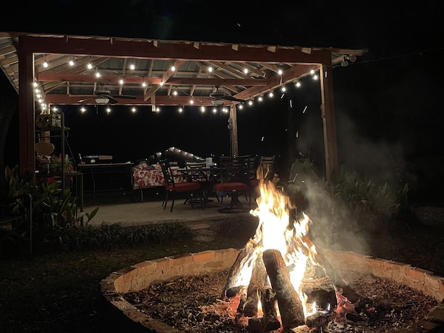 yard at night featuring a patio area, ceiling fan, and an outdoor fire pit