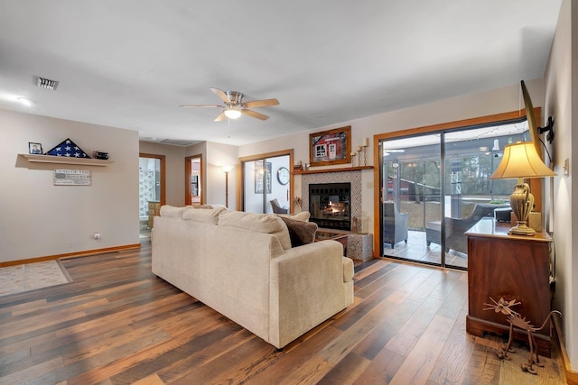 living room featuring dark wood-type flooring, ceiling fan, and a tile fireplace