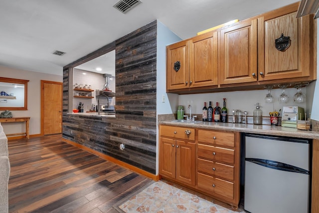 bar featuring wood-type flooring, sink, stainless steel fridge, and wooden walls