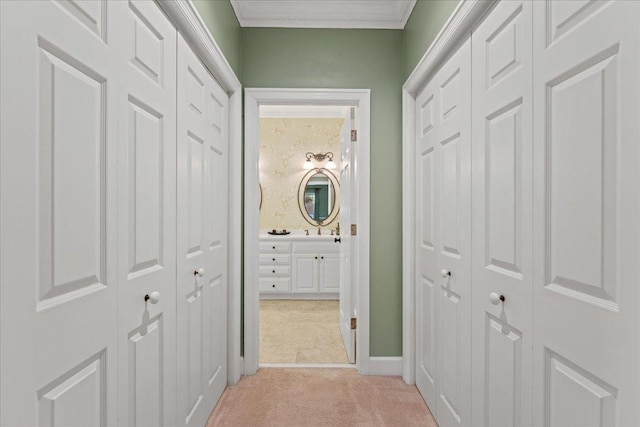 corridor with crown molding, sink, and light carpet