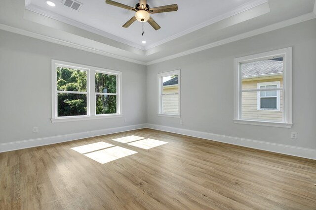 empty room with light wood-style floors, baseboards, a raised ceiling, and visible vents