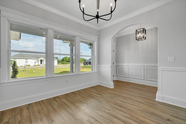 unfurnished dining area featuring arched walkways, a wainscoted wall, light wood-style flooring, and a chandelier