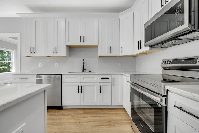 kitchen featuring appliances with stainless steel finishes, light stone counters, a sink, light wood finished floors, and white cabinetry