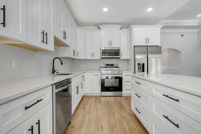 kitchen featuring light stone countertops, appliances with stainless steel finishes, a sink, light wood-style floors, and white cabinetry