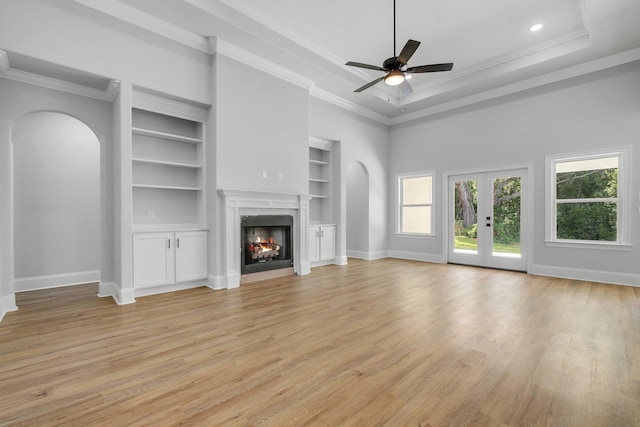 unfurnished living room featuring arched walkways, baseboards, light wood-style flooring, and a high end fireplace