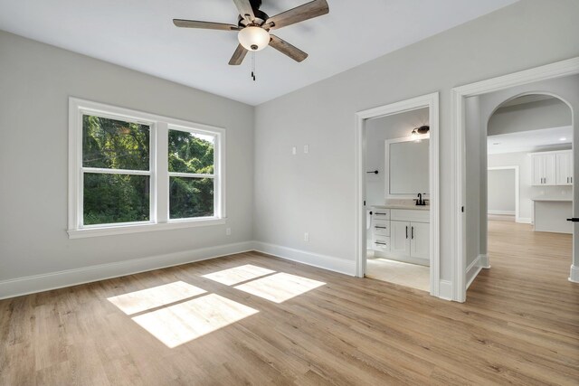 spare room with a ceiling fan, baseboards, arched walkways, and light wood finished floors