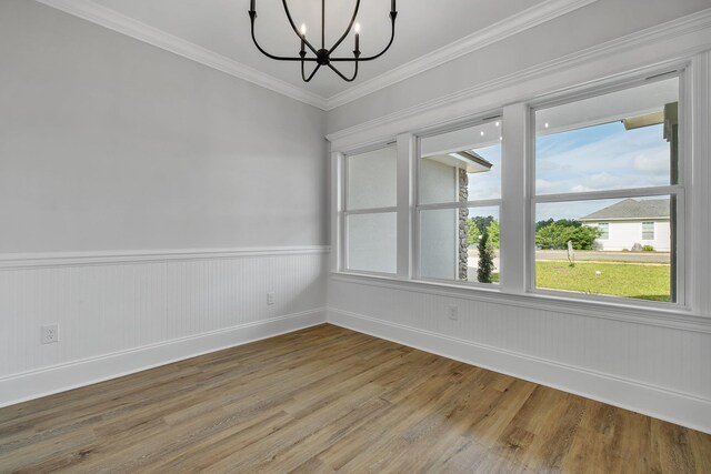 unfurnished room featuring an inviting chandelier, wainscoting, baseboards, light wood-type flooring, and ornamental molding