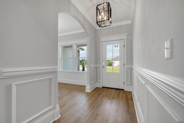 foyer entrance with crown molding, arched walkways, wainscoting, wood finished floors, and a chandelier