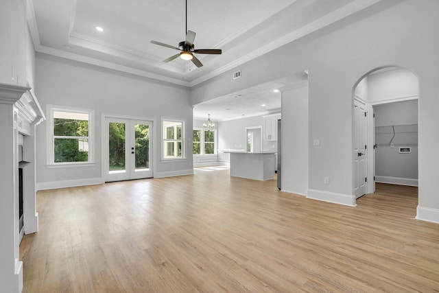 unfurnished living room featuring a fireplace, arched walkways, ceiling fan with notable chandelier, light wood-type flooring, and ornamental molding