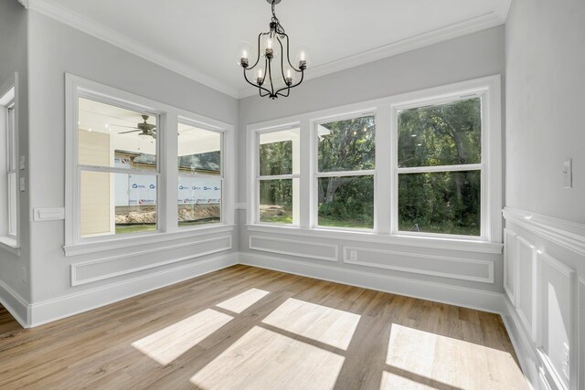 unfurnished dining area featuring a decorative wall, ornamental molding, ceiling fan with notable chandelier, and light wood-style floors