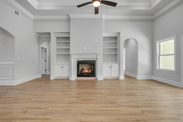 unfurnished living room featuring arched walkways, ceiling fan, ornamental molding, and light wood-style flooring