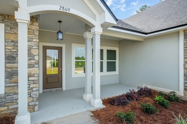 property entrance featuring covered porch, a shingled roof, stone siding, and stucco siding