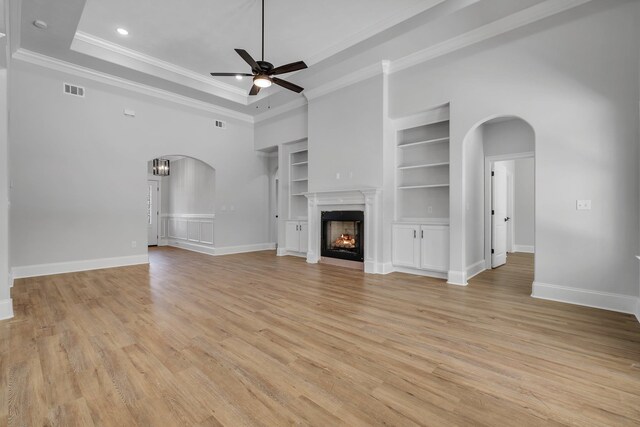 unfurnished living room with arched walkways, ceiling fan, baseboards, and built in shelves