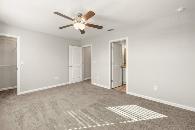 unfurnished bedroom featuring a closet, light colored carpet, ceiling fan, and ensuite bath