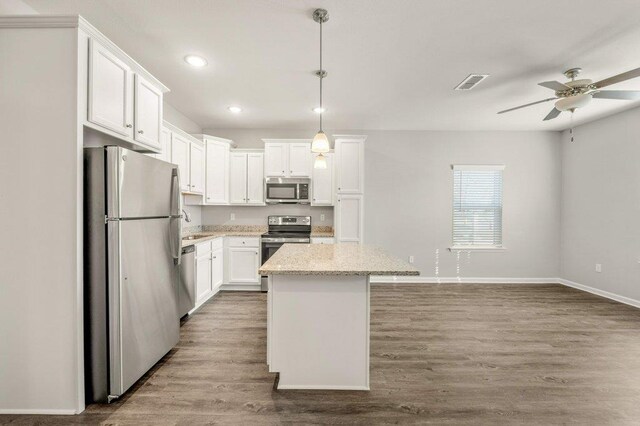 kitchen featuring wood-type flooring, stainless steel appliances, hanging light fixtures, white cabinets, and a center island