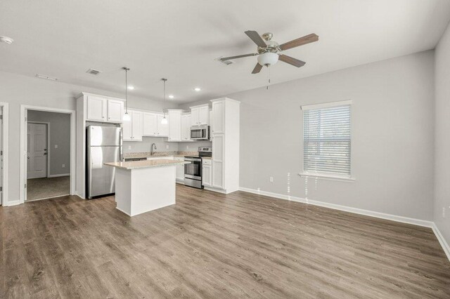 kitchen with wood-type flooring, appliances with stainless steel finishes, decorative light fixtures, white cabinets, and a center island