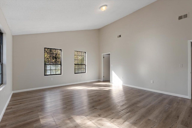 empty room with a textured ceiling, dark hardwood / wood-style flooring, and high vaulted ceiling