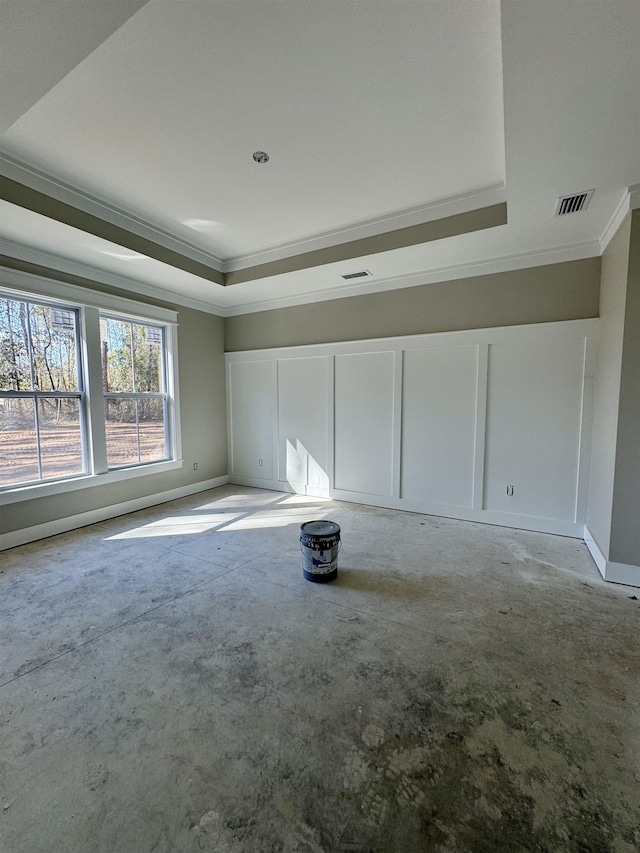 empty room with concrete flooring, a decorative wall, baseboards, a tray ceiling, and crown molding