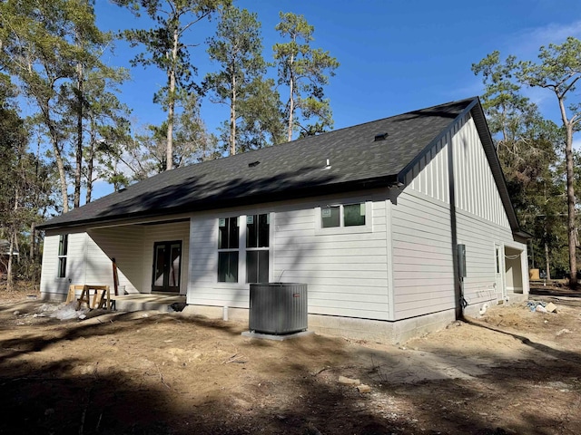 rear view of house featuring cooling unit and roof with shingles