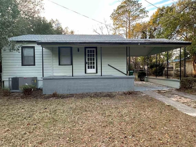 view of front facade featuring covered porch, a carport, a shingled roof, and central air condition unit