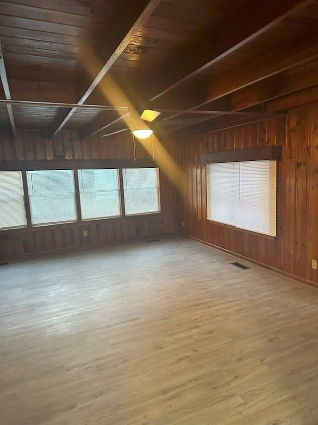 spare room with light wood finished floors, visible vents, and wood walls