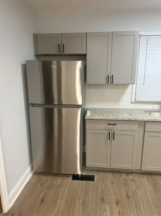 kitchen featuring freestanding refrigerator, backsplash, light wood-style flooring, and gray cabinetry