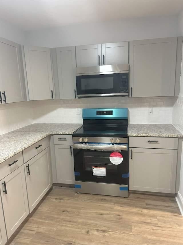 kitchen with stainless steel appliances, light wood-style flooring, and tasteful backsplash