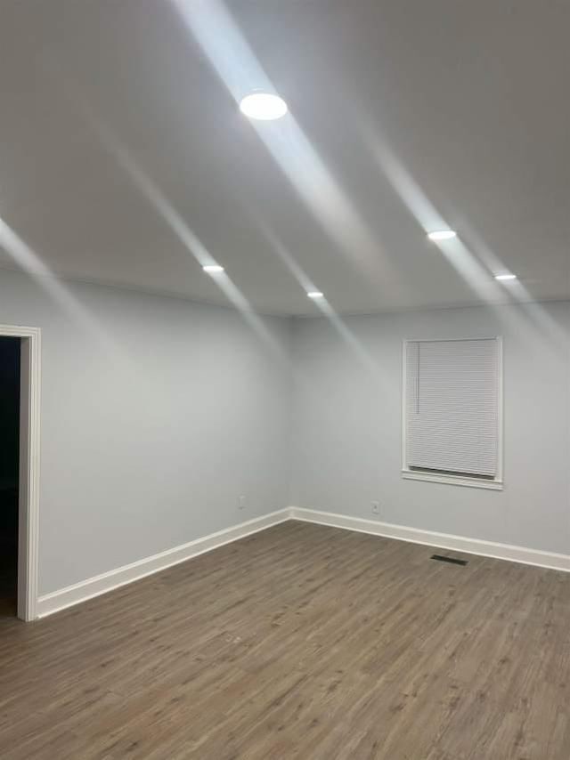 interior space with dark wood-style floors, vaulted ceiling, visible vents, and baseboards