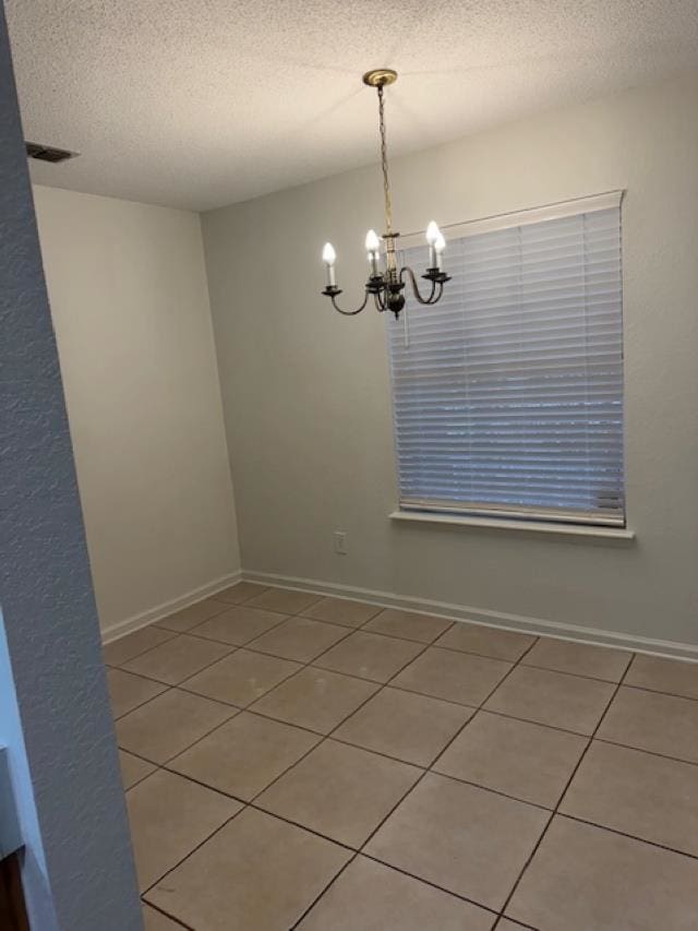 empty room featuring tile patterned floors, a notable chandelier, and a textured ceiling