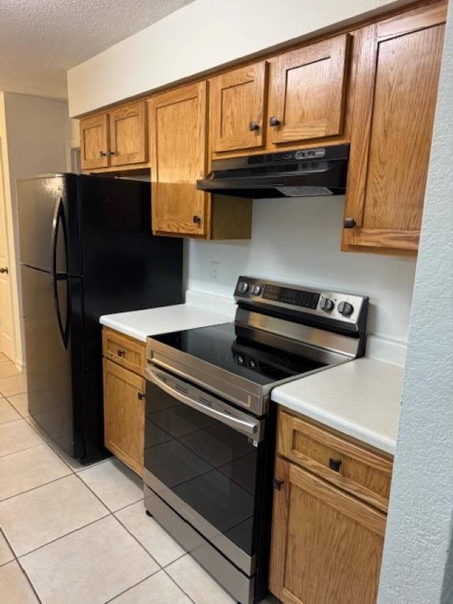 kitchen with stainless steel electric range oven, black refrigerator, light tile patterned floors, and a textured ceiling