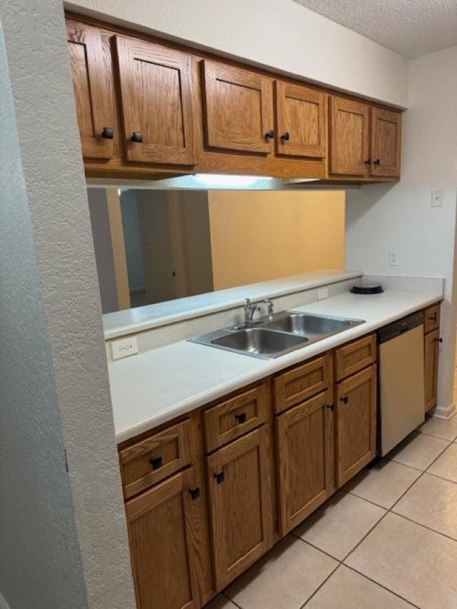 kitchen with sink, light tile patterned floors, stainless steel dishwasher, and a textured ceiling