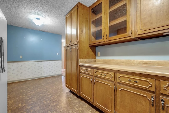 820 Essex Dr, Tallahassee, FL 32304 - kitchen with brown cabinetry, light countertops, a textured ceiling, wallpapered walls, and glass insert cabinets
